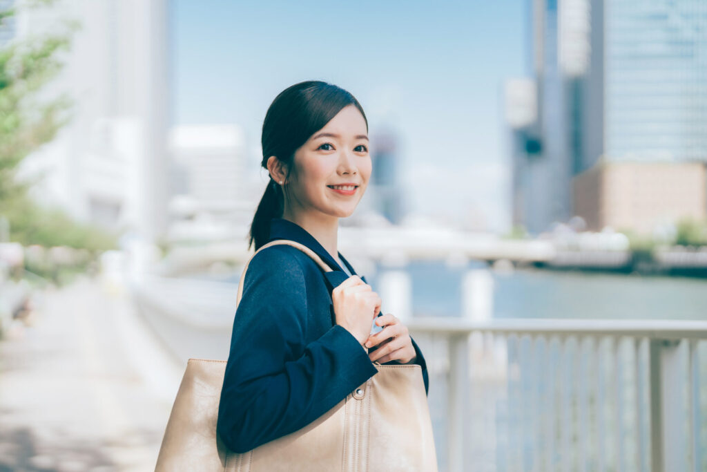 川沿いをバックを持ちながら笑顔を見せて歩く女性社員