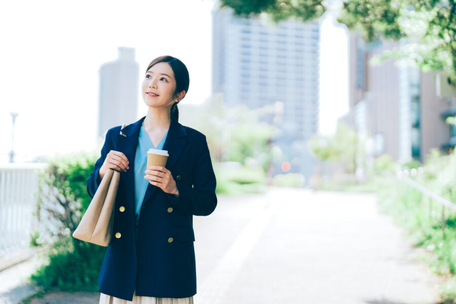 コーヒーを持ちながら笑顔でオフィスを後にする自分らしいキャリアを目指す女性。自分らしい働き方を実現するCalmee（カーミー）のキャリアコーチング